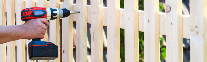 Akkuschrauber in der Hand einer Person, die einen Gartenzaun aus Holz zusammenbaut